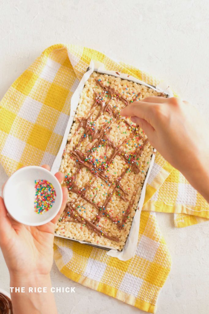 Decorating rice bubble slice with chocolate and sprinkles.