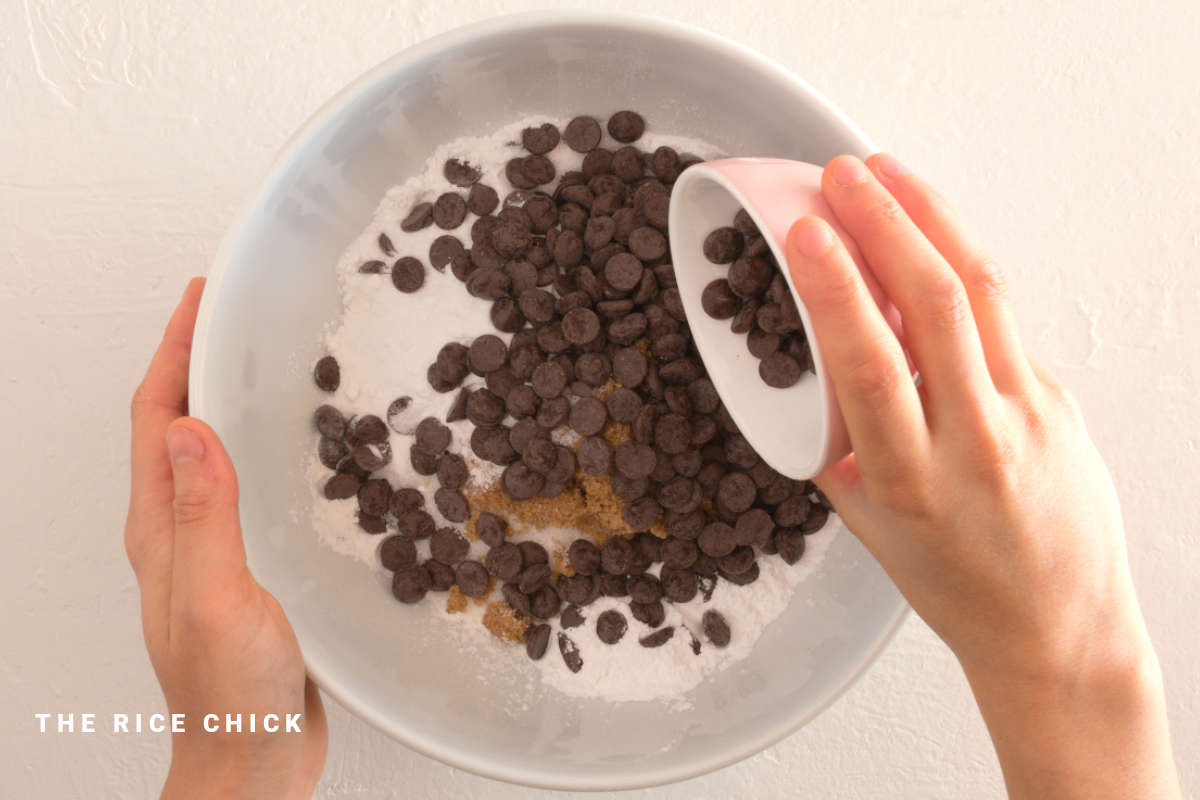 Placing chocolate chips into a white mixing bowl for chocolate chip muffins.