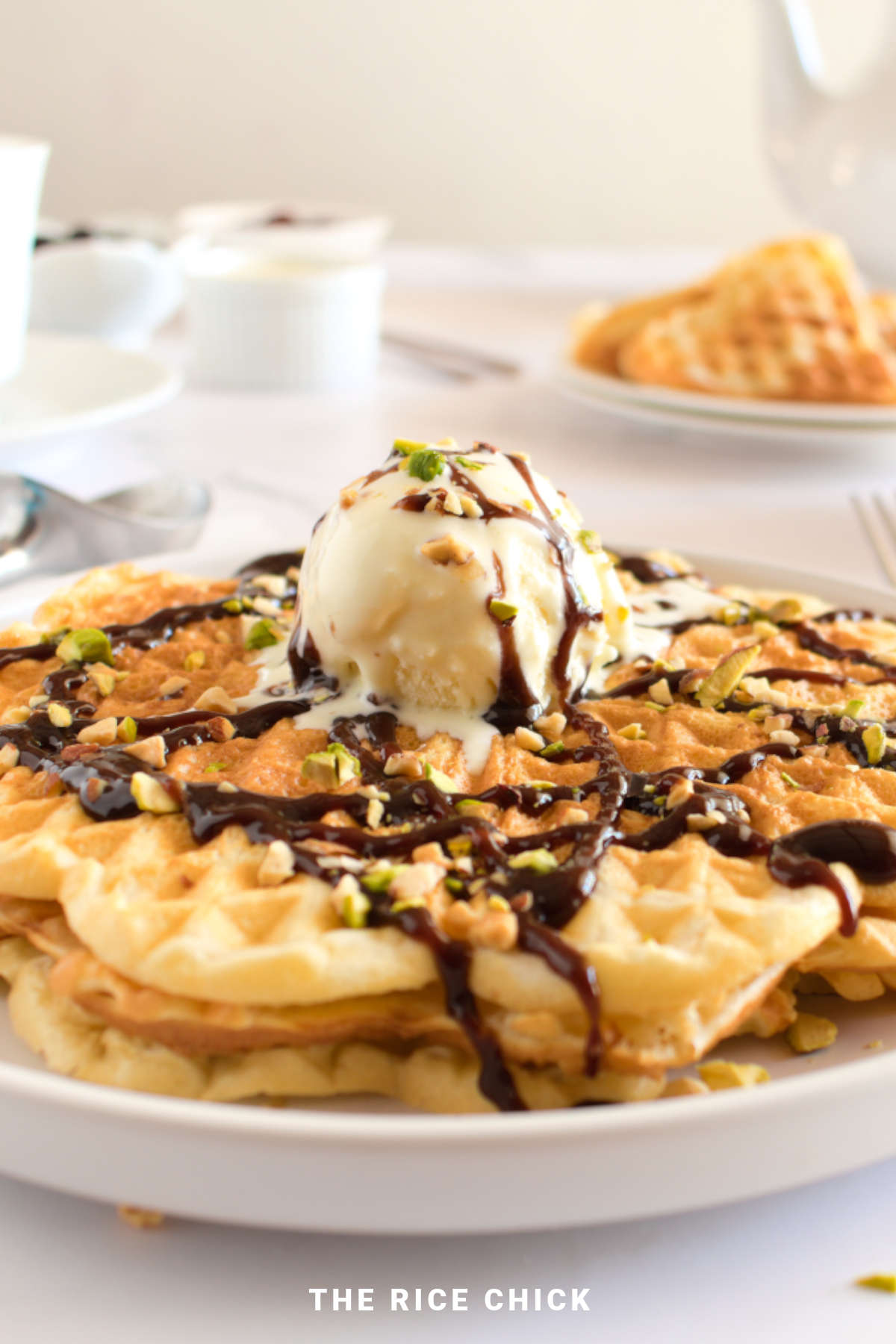 A stack of mochi waffles on a plate topped with a scoop of ice cream and chocolate sauce.