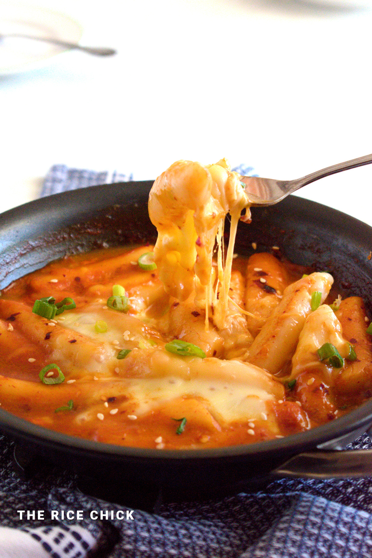 Tteokbokki with melted cheese on top in a pan.