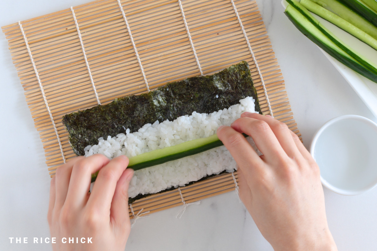 Placing a strip of cucumber on sushi rice.