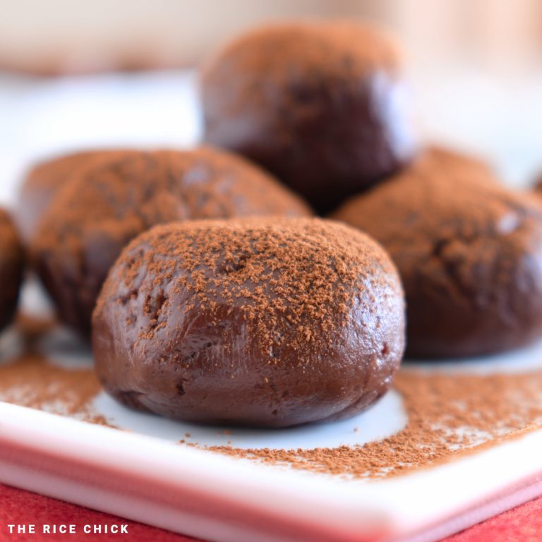 Close up image of chocolate mochi dusted with cocoa powder on a white plate.
