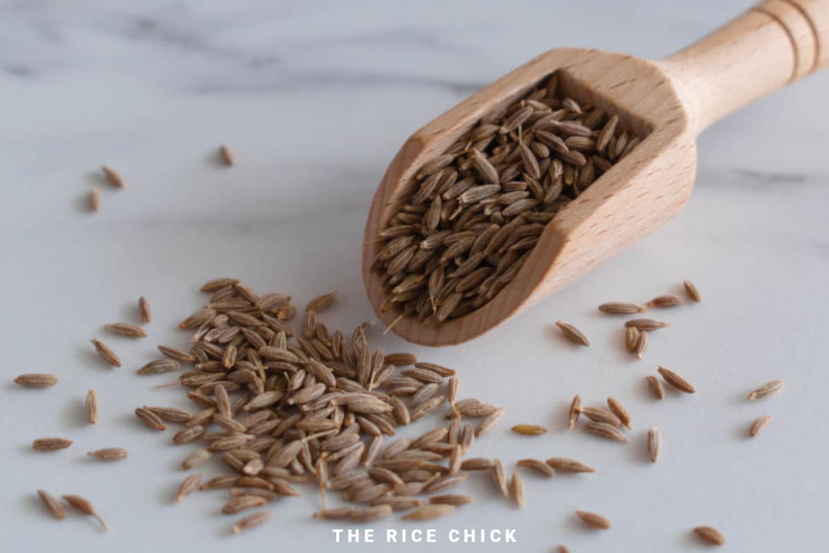 Cumin seeds in a wooden scoop.