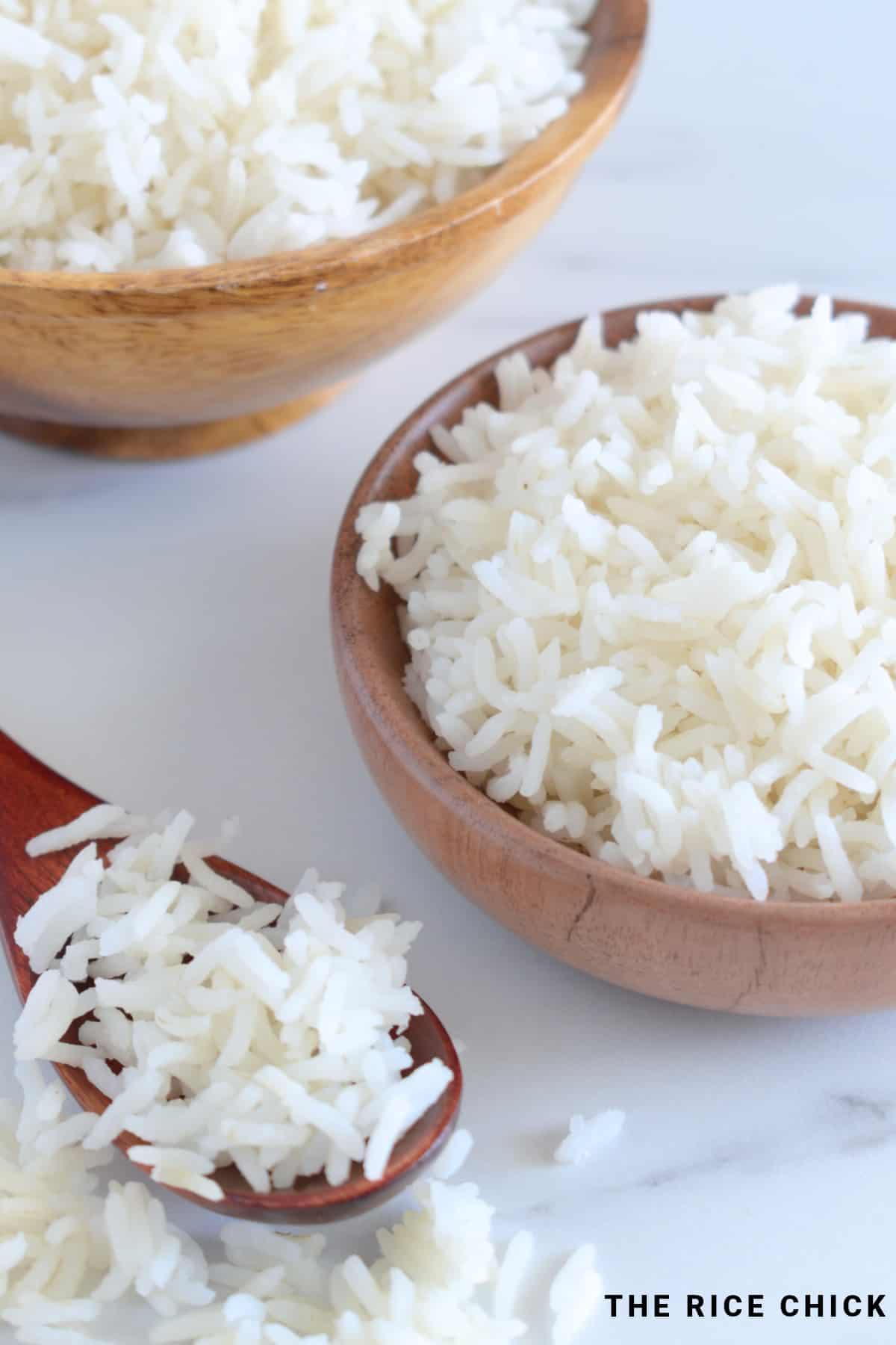 Cooked basmati rice in wooden bowls, and a wooden spoon with basmati rice on it.