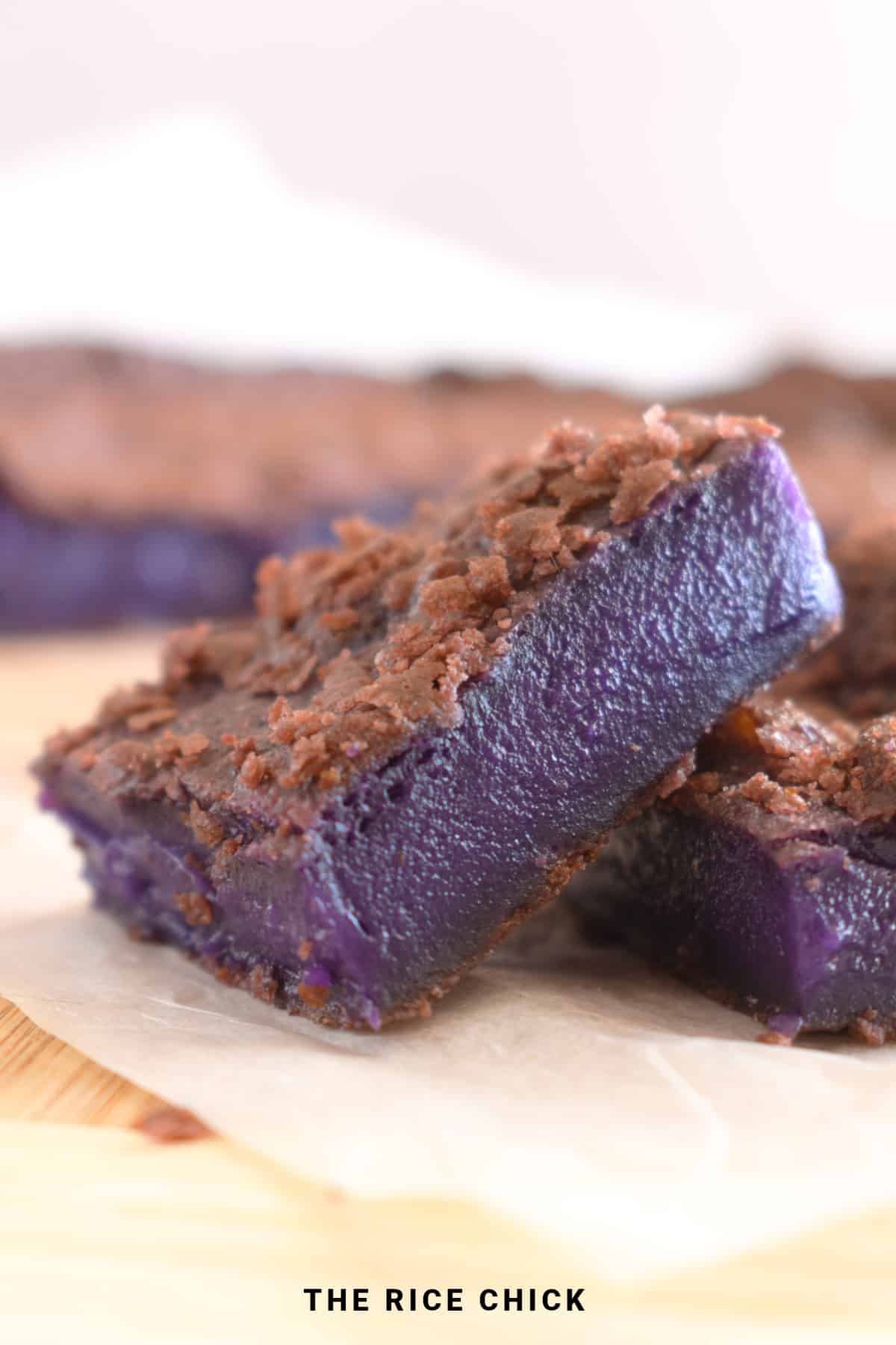 A piece of ube butter mochi on a wooden board and parchment paper.