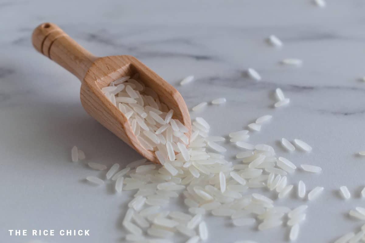 Uncooked jasmine rice in a wooden scoop.