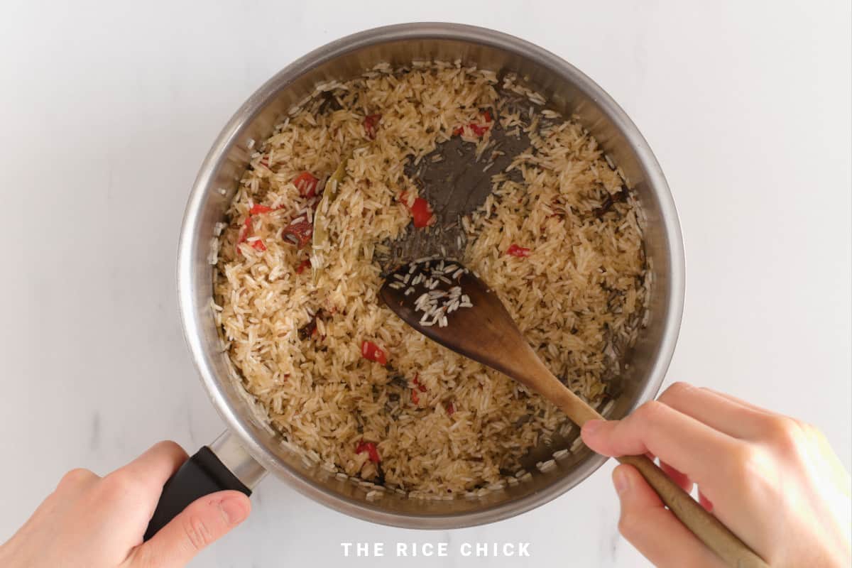 Mixing rice and spices in a saucepan for jeera rice.