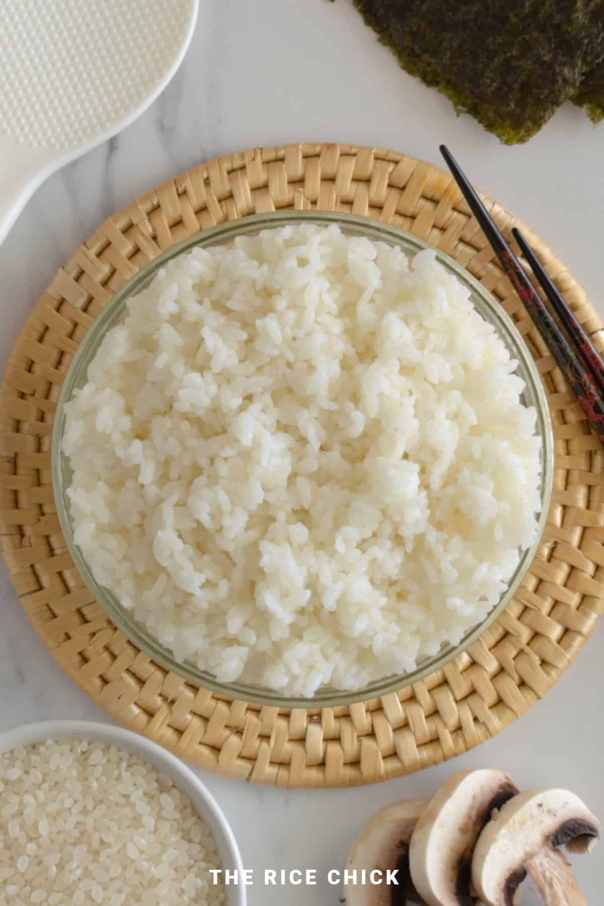 Sushi rice in a glass bowl on a round woven mat.