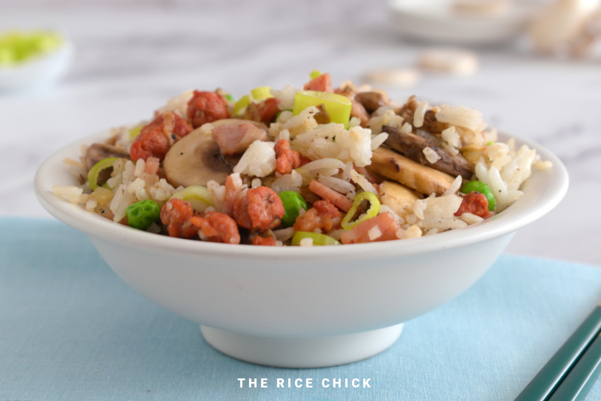 Close up image of fried rice with chorizo in a white bowl on a blue napkin.