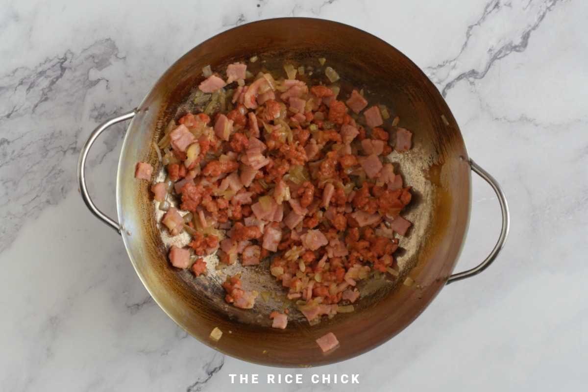 Chorizo, bacon, and onion pieces in a wok.