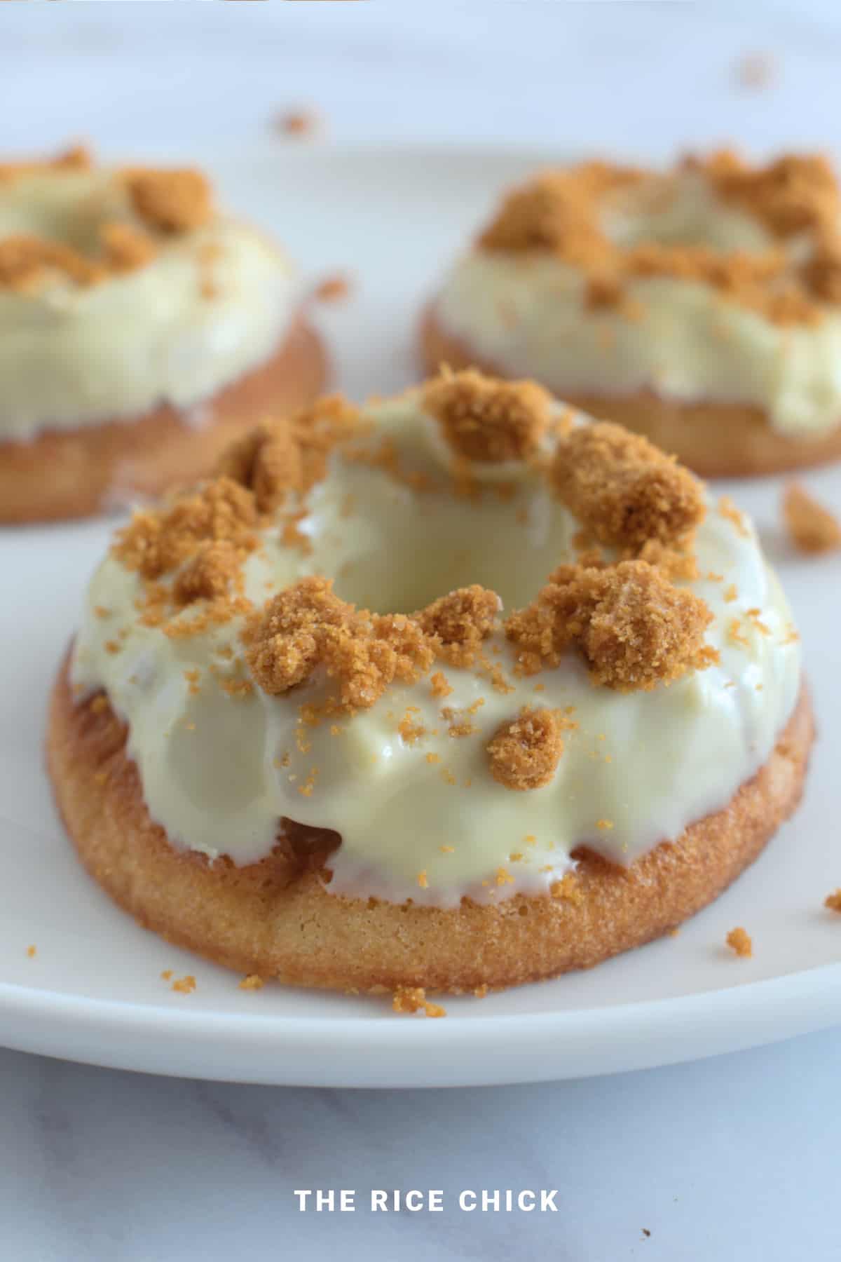 Chocolate glazed baked mochi donuts topped with crushed biscuits on a white plate.