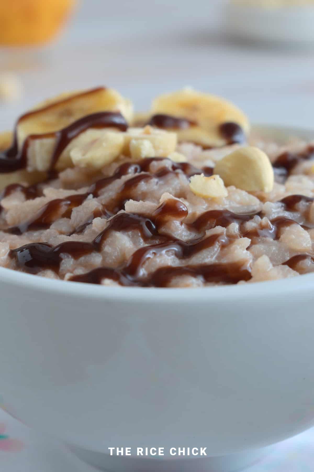 Nutella rice flakes porridge with chocolate sauce, chopped nuts, and sliced banana in a white bowl.