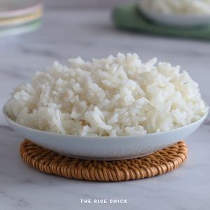 Cooked basmati rice in a shallow white bowl on a woven coaster.