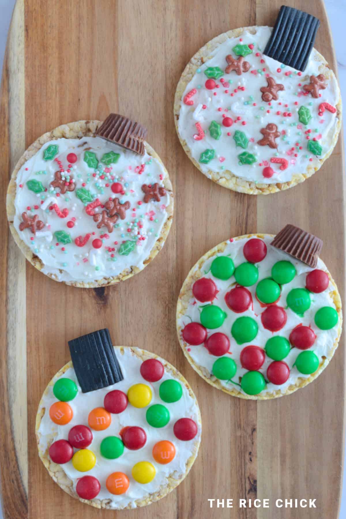 Christmas ornaments made from rice cakes, M&M's, and Christmas sprinkles on a wooden board.