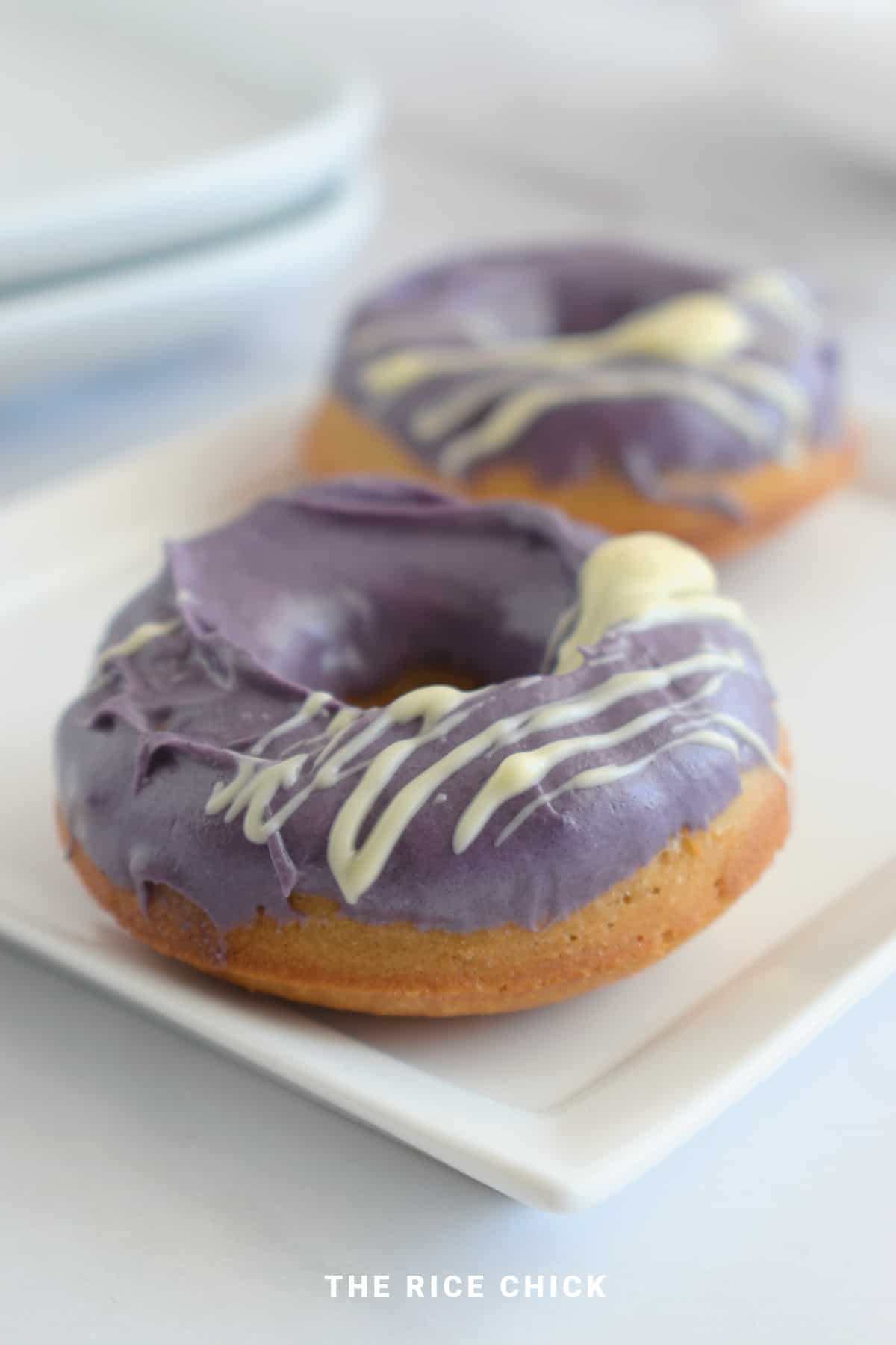 Two mochi donuts with ube white chocolate glaze on top on a white plate.