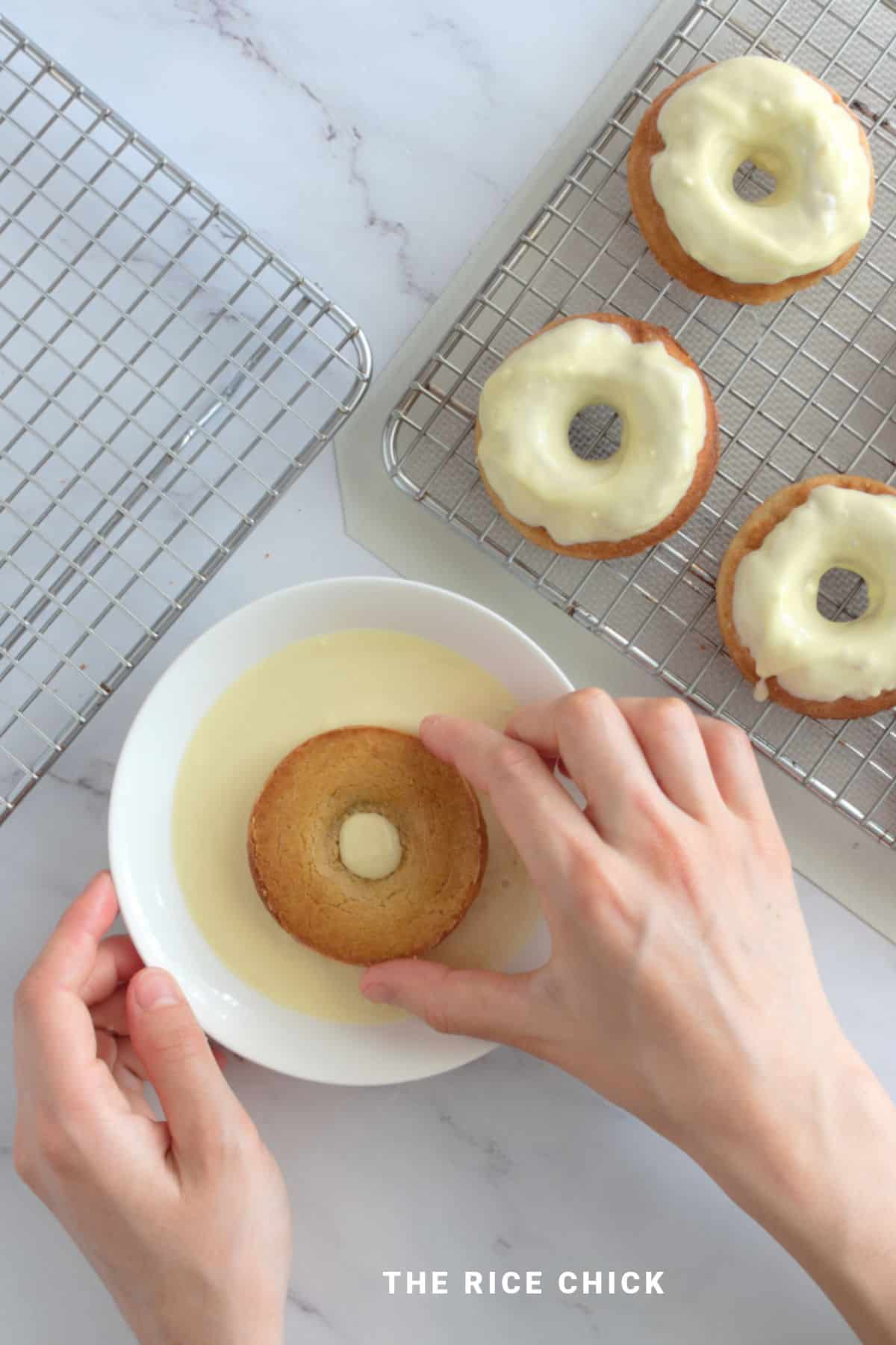 Dipping baked donut into white chocolate glaze.