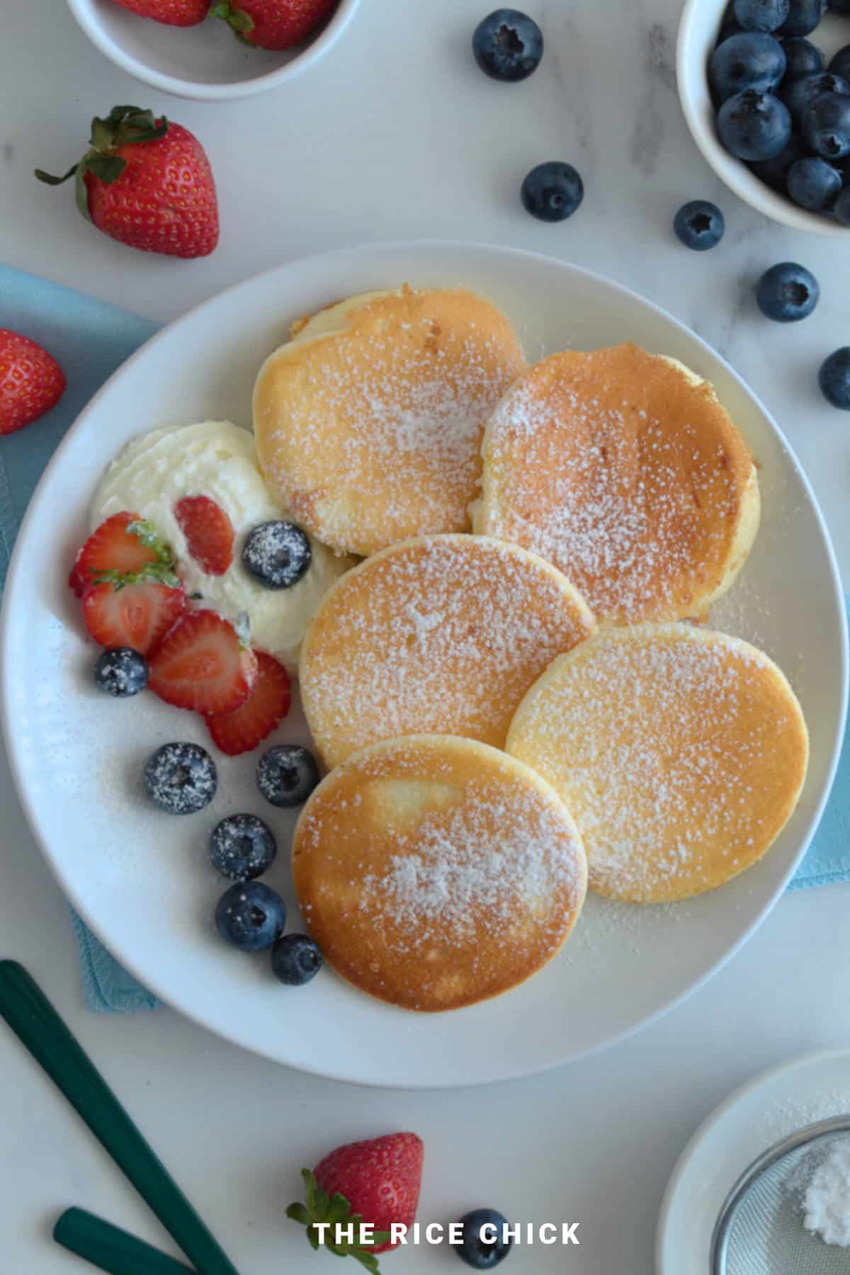 A plate of rice flour pancakes with blueberries, whipped cream, and strawberries.
