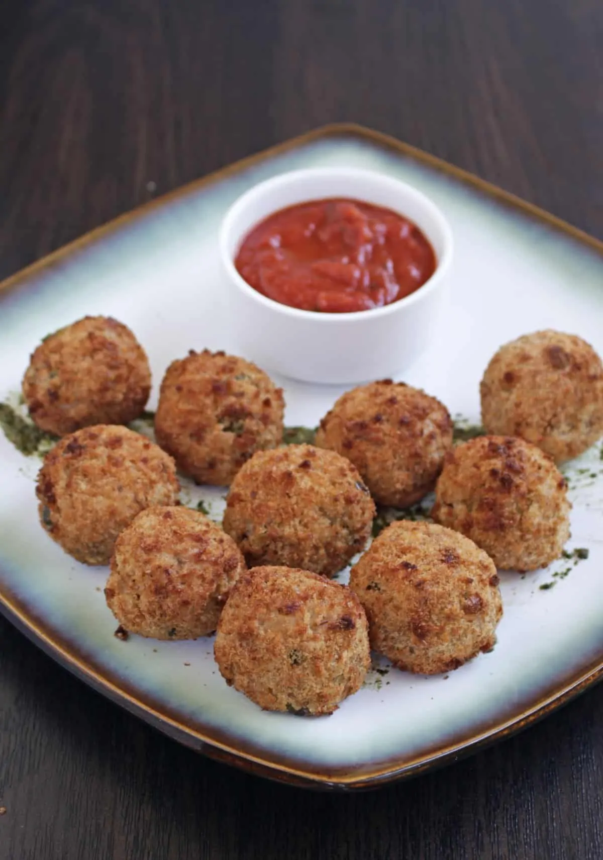 Arancini on a square white plate with tomato sauce in a dipping bowl.