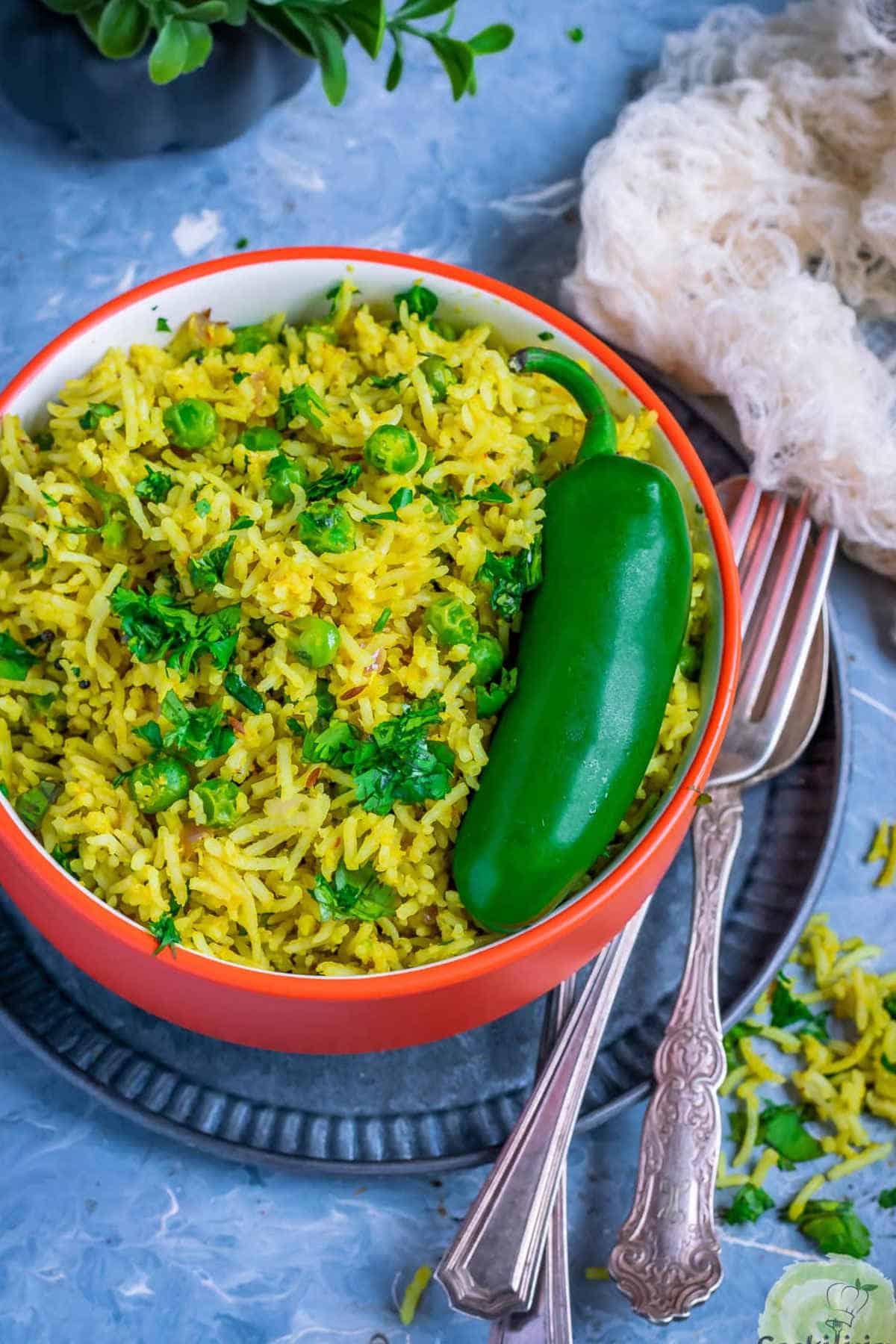 Green peas pulao in a red bowl with a green chili on top.