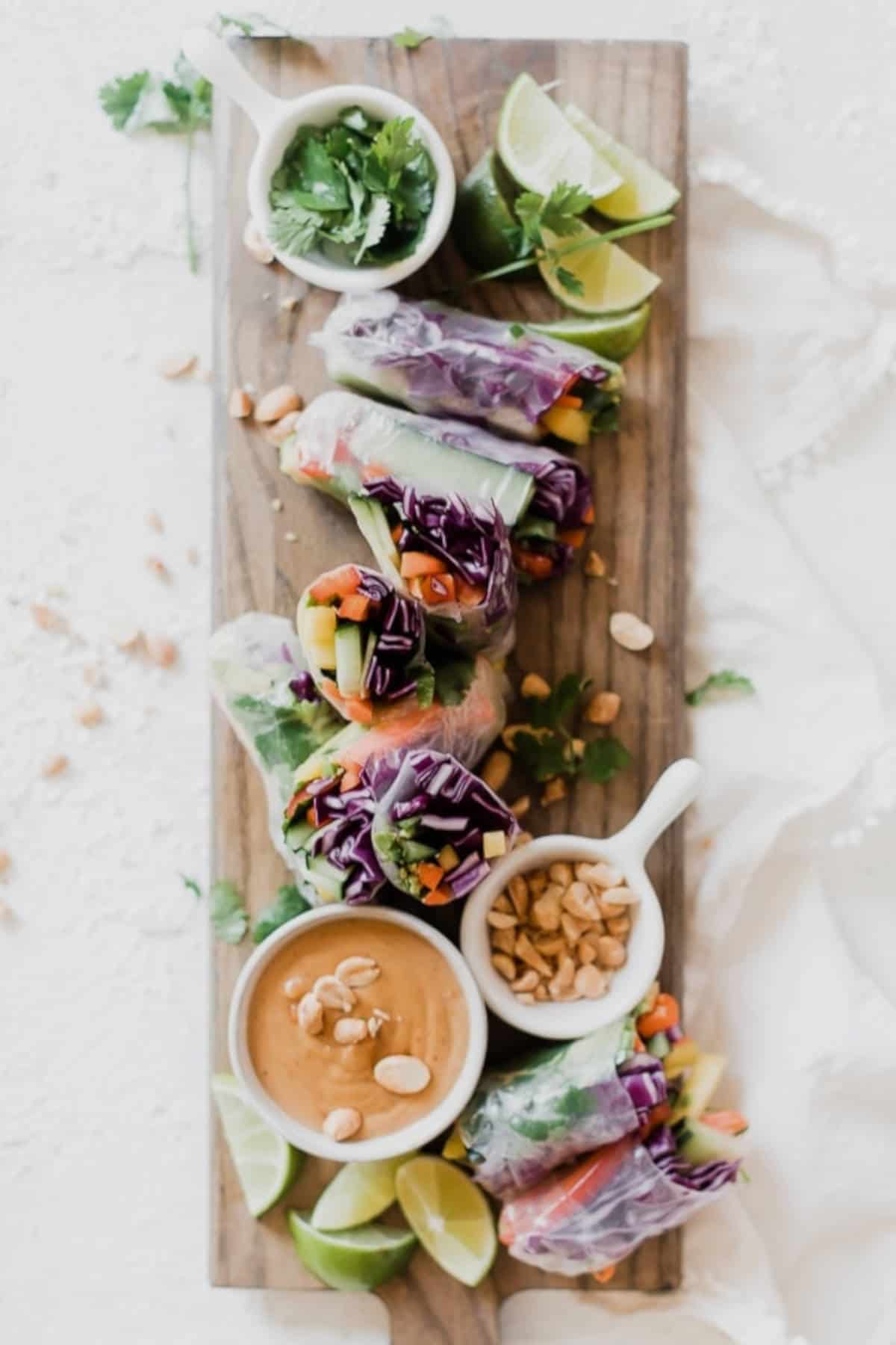 Manga salsa summer rolls on a wooden board with peanuts, lime, coriander, and peanut sauce.