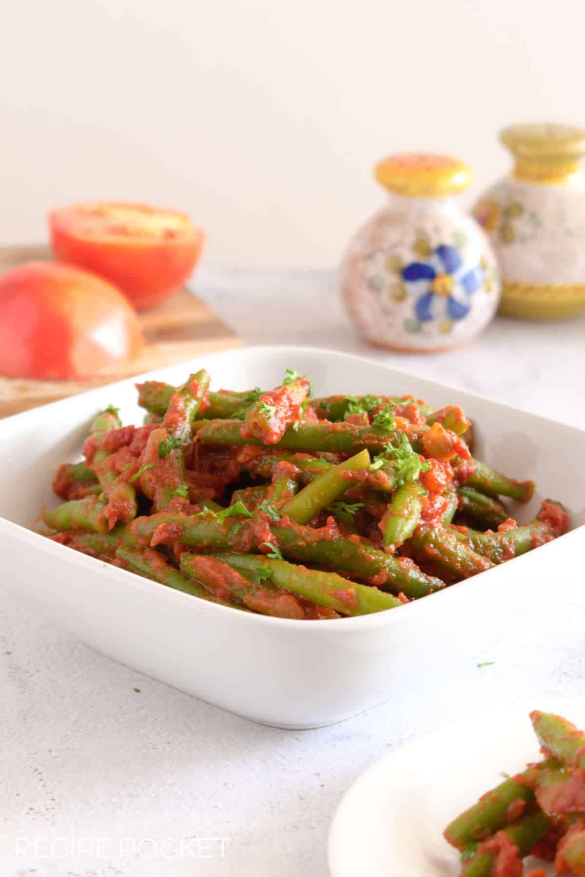 Green beans in tomato sauce in a square white bowl.