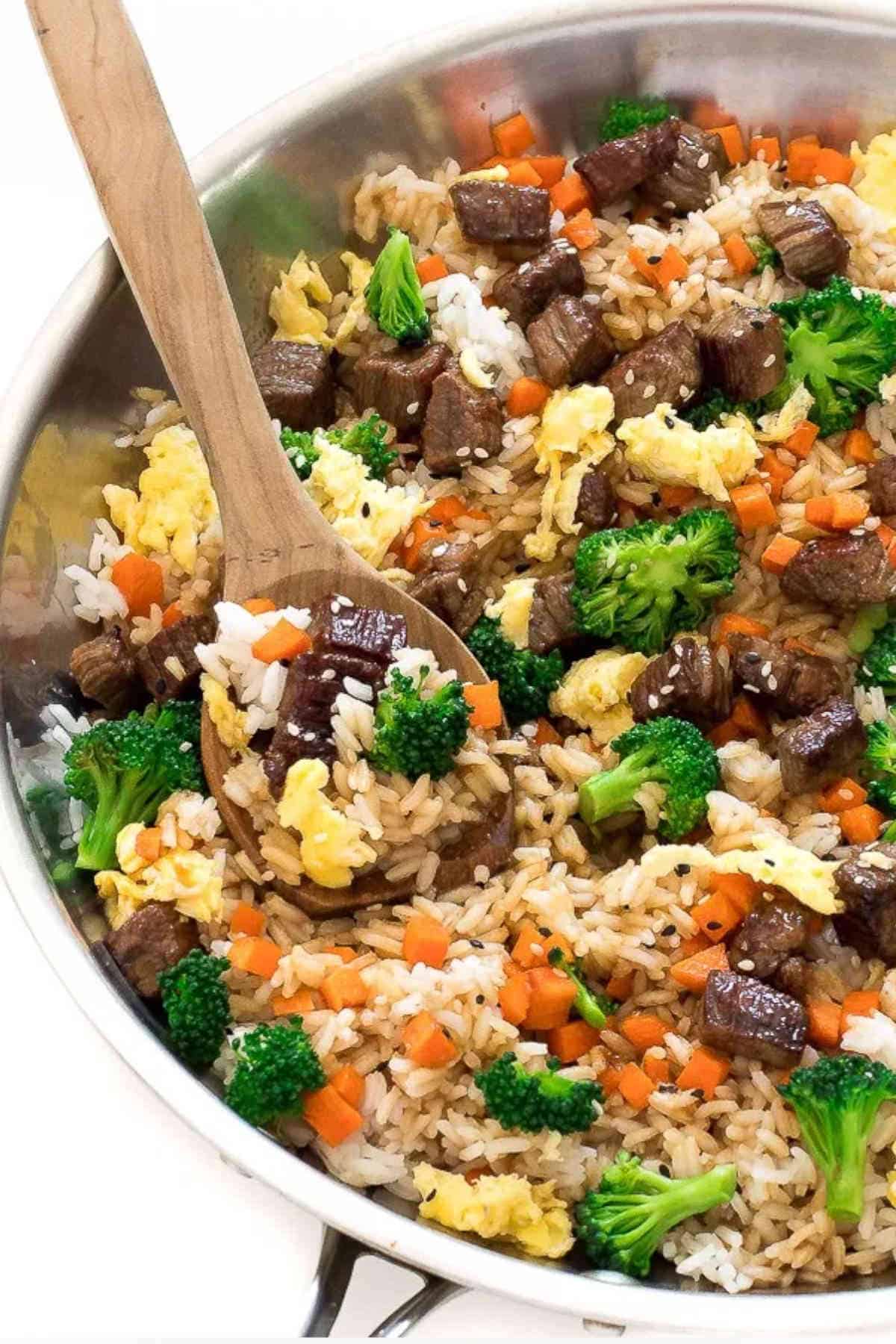 Close up image of beef fried rice in a pan with a wooden spoon.