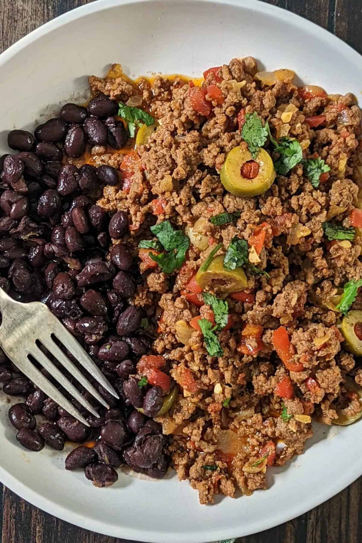 Beef picadillo on a white plate with beans.