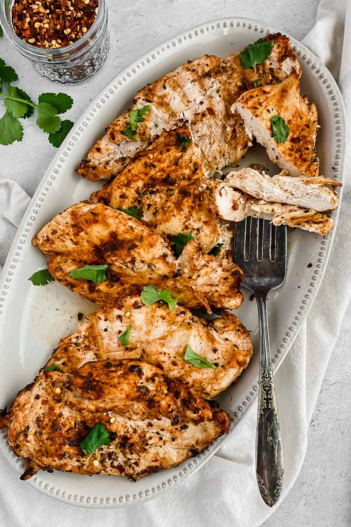 Close up image of grilled chicken on an oval plate with a fork.