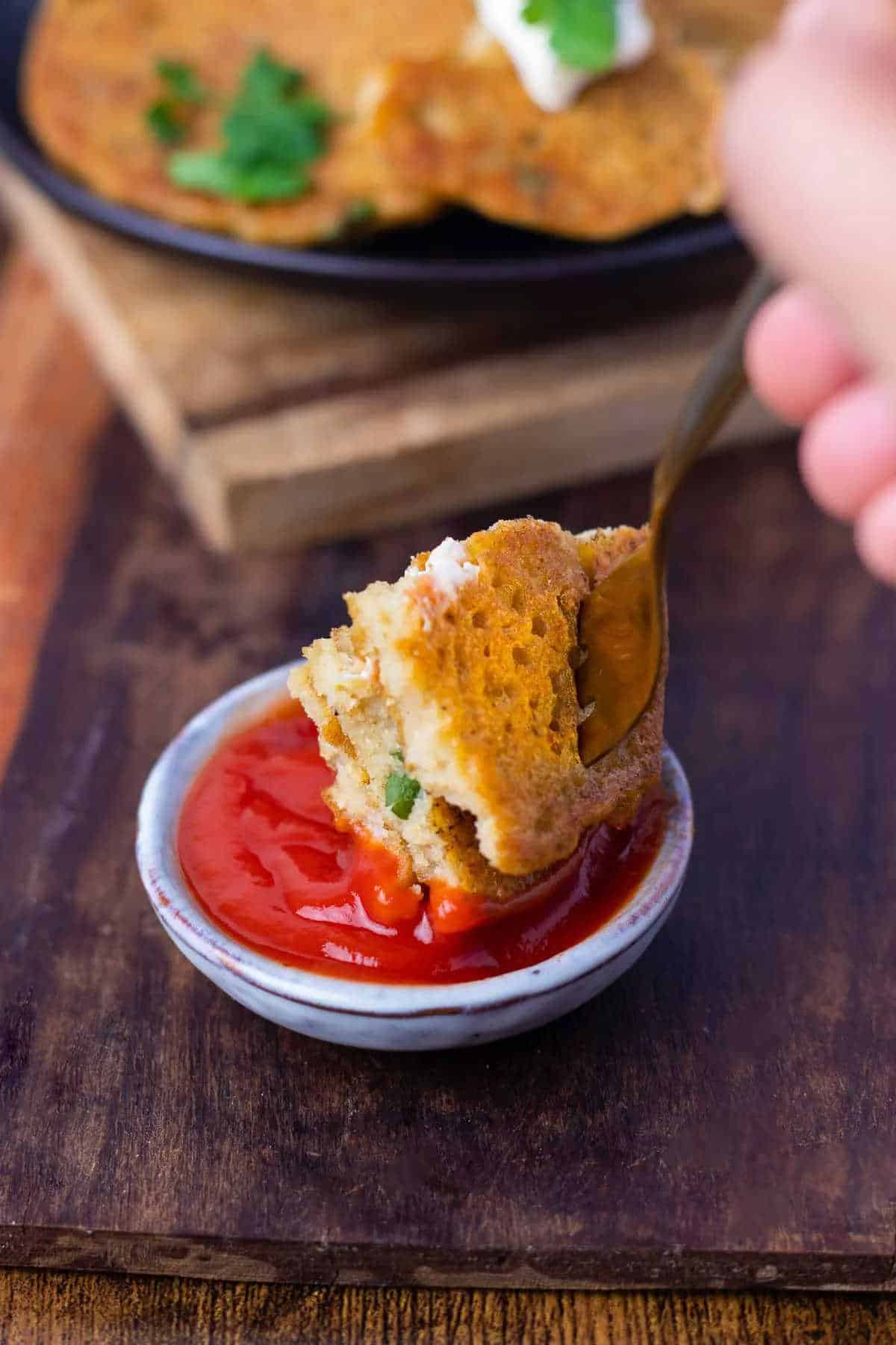 A slice of lentil pancake on a fork being dipped into tomato sauce.