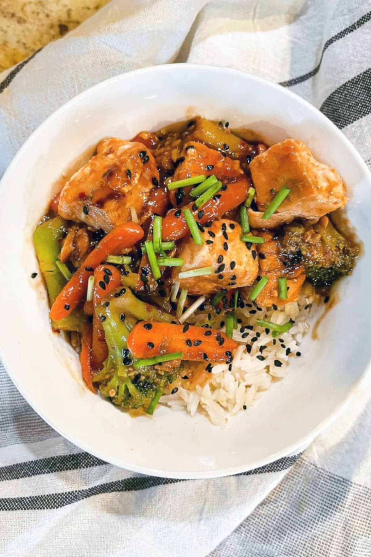 Salmon, green onions, carrots, broccoli, and rice in a white bowl.