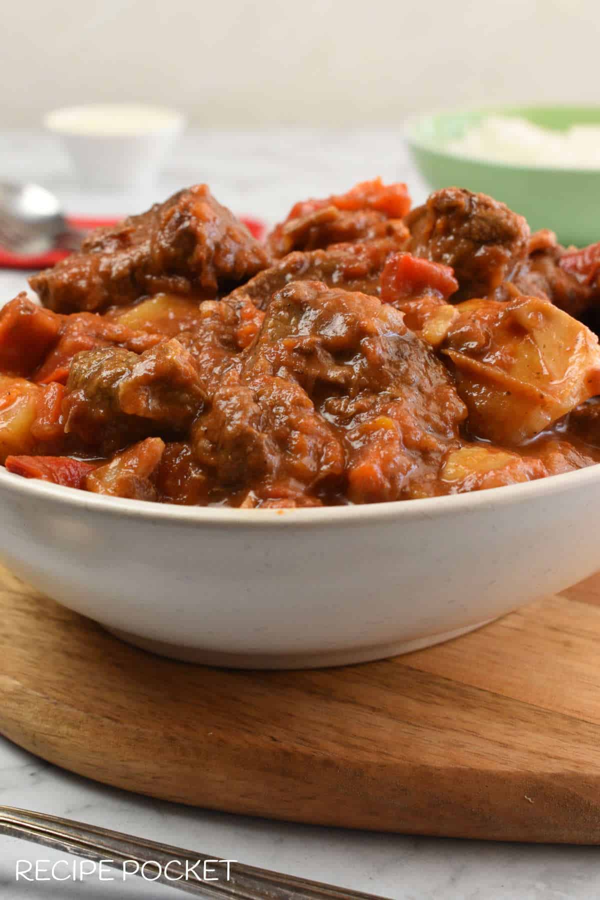 Slow cooker Hungarian goulash in a white bowl on a wooden board.