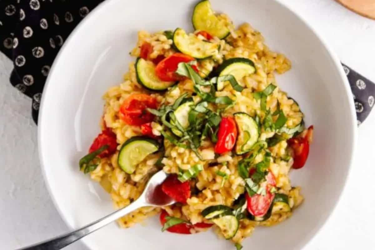 Close up image of risotto with zucchini and cherry tomatoes on a plate with a fork.