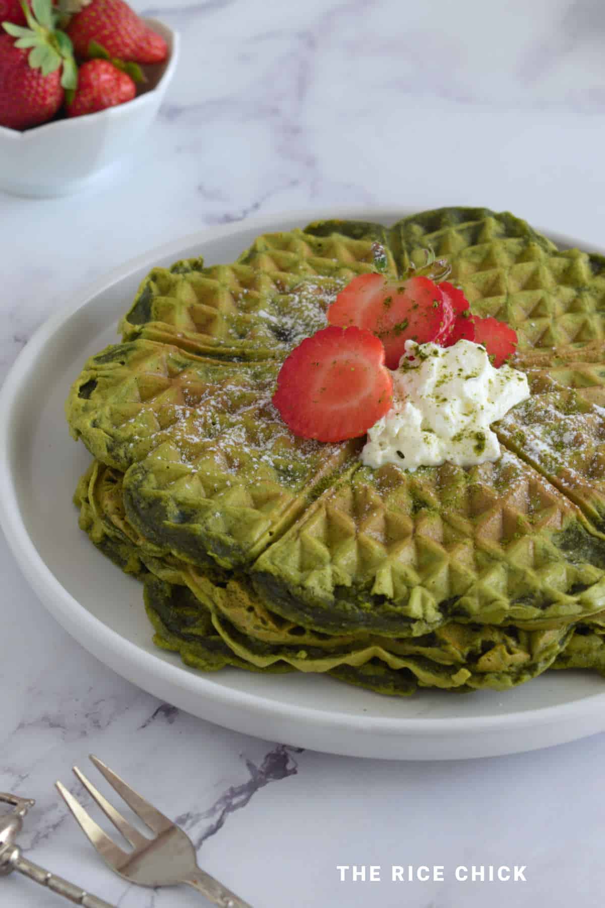 Stack of matcha waffles topped with strawberries and cream.