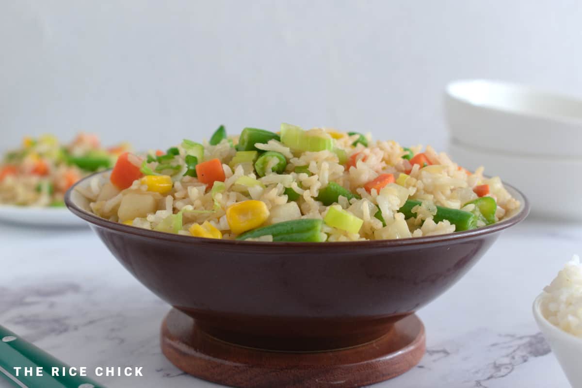 Close up image of fried rice in a bowl on a wooden board.