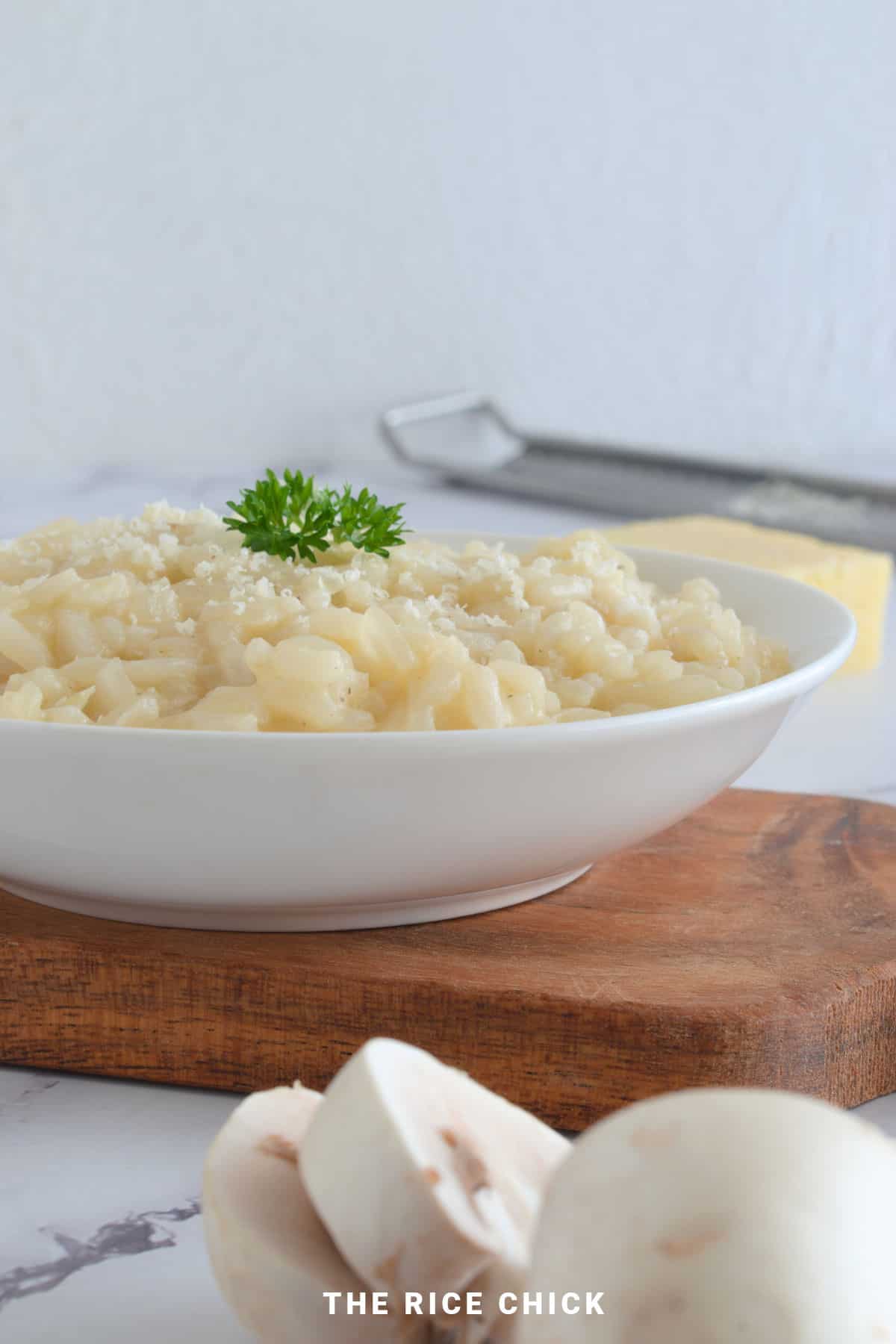 Close up image of risotto with grated parmesan and parsley in a white bowl.