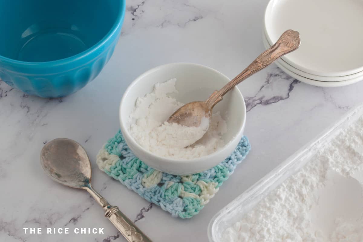 Close up image of rice flour in a white bowl with a spoon.