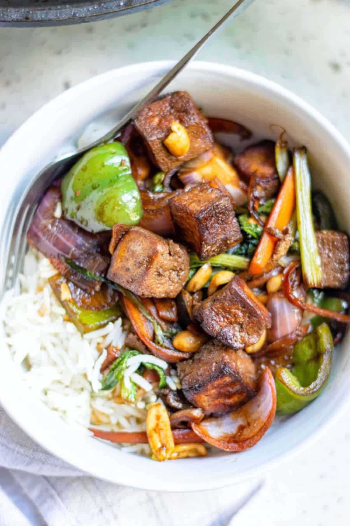 Kung pao tofu in a white bowl with a fork.