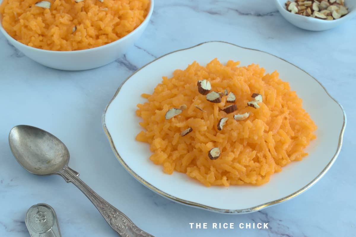 Close up image of orange sweet rice on a plate with chopped nuts on top.