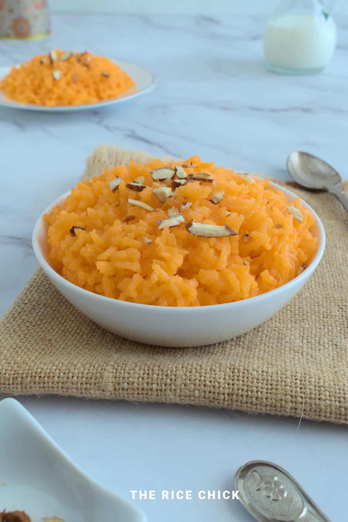 Orange rice in a bowl with chopped nuts on top.