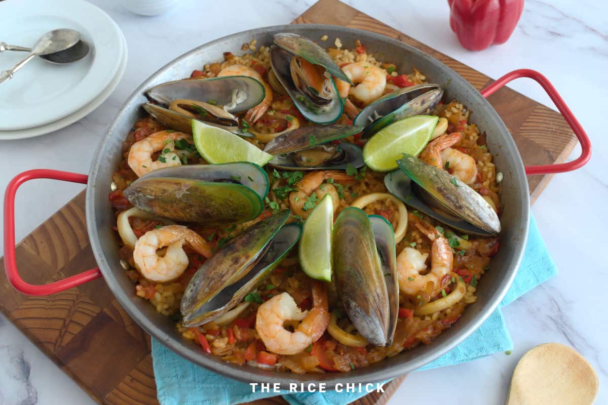 Close up image of paella in a paella pan with lime wedges.