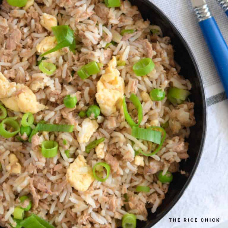 Tuna fried rice in a black bowl garnished with spring (green) onions.