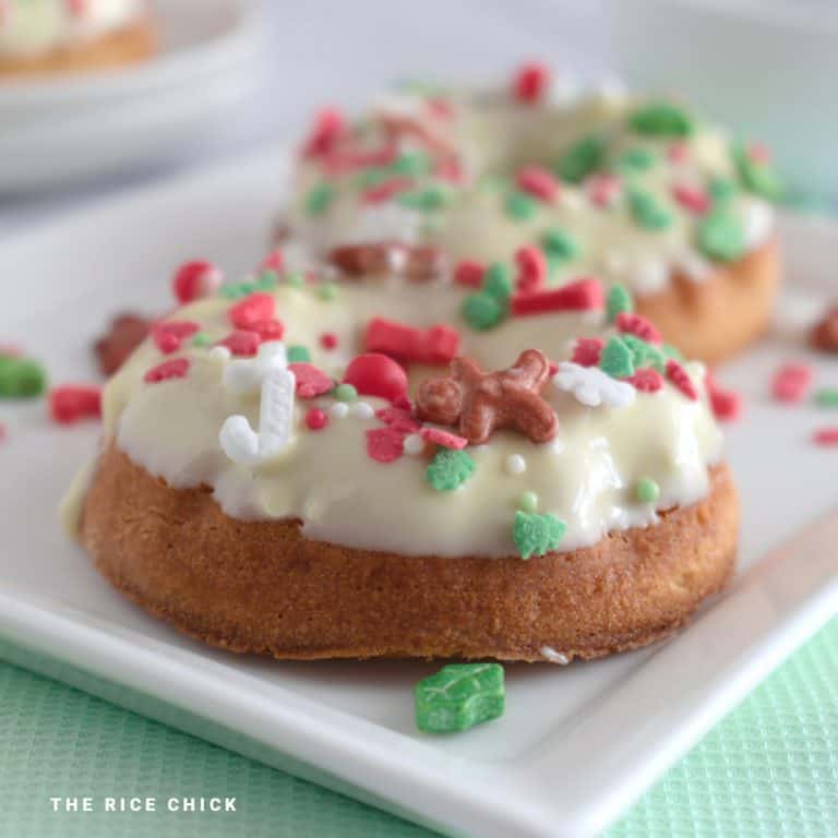 Two baked mochi donuts glazed with white chocolate and Christmas sprinkles on a white plate.
