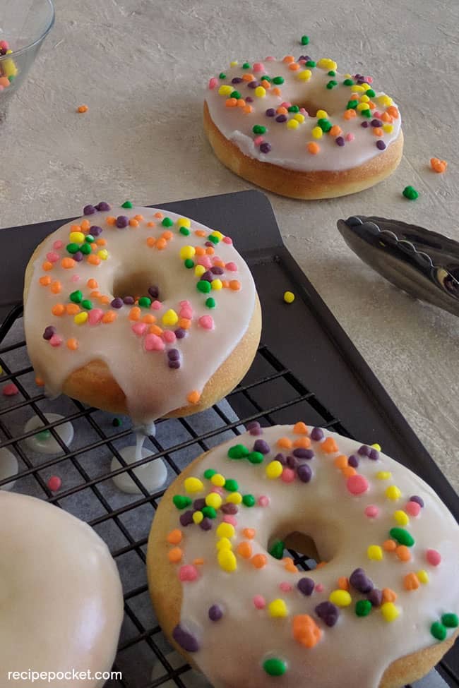 Baked mochi donuts with colored sprinkles on top on a wire rack.