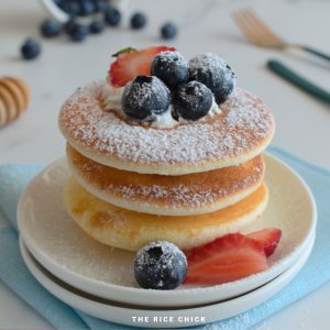 A stack of three rice flour pancakes with strawberries and blueberries on a white plate.