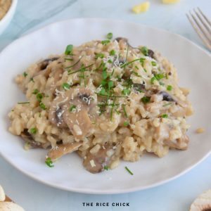 Close up image of risotto ai funghi on a plate garnished with chopped chives and grated parmesan.
