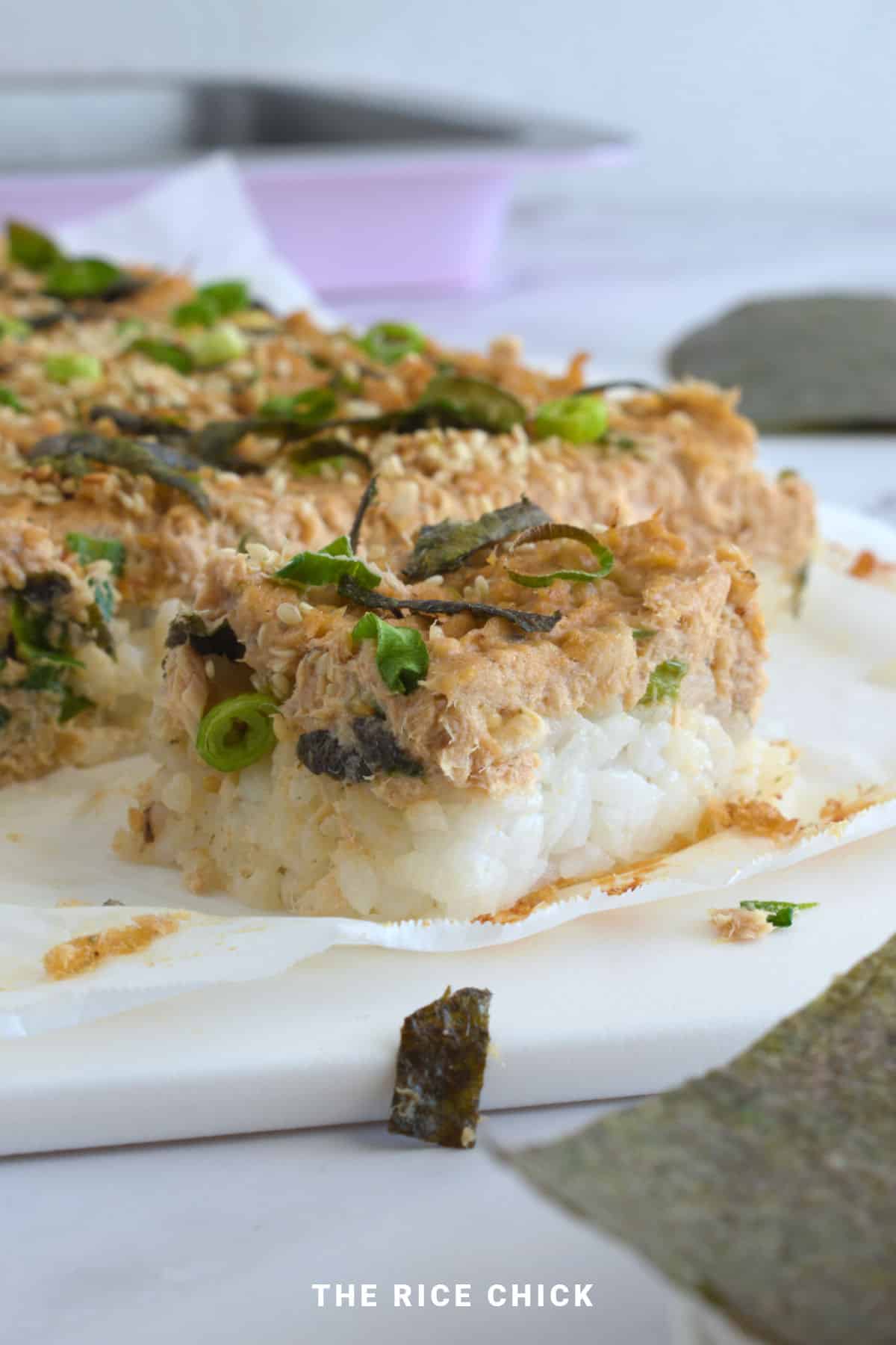 Close up image of a slice of salmon sushi bake on a white board.