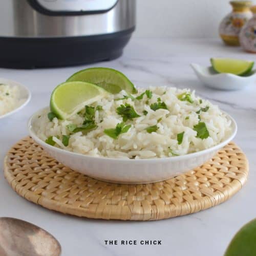 Lime and cilantro rice in a white bowl with lime wedges on top.